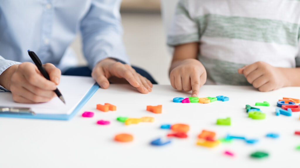 Private child lessons. Little boy counting colorful numbers, studying with professional woman therapist at office